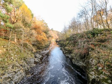 A river flowing between rocky banks with trees on both sides in autumn at Badgers Sett in Winston near Staindrop