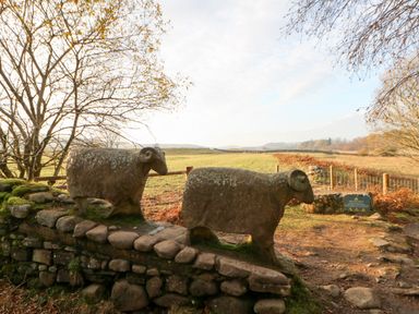 Two stone sculptures of rams on a stone wall with a grassy field and trees in the background at Badgers Sett Winston near Staindrop