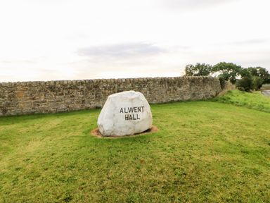 A large stone with Alwent Hall text on grass near a stone wall and trees at Badgers Sett in Winston near Staindrop