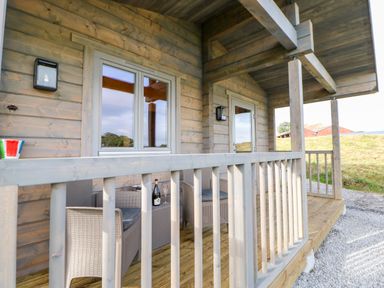 A wooden porch with wicker chairs a table a wine bottle and glass at Badgers Sett in Winston near Staindrop