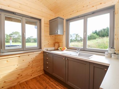 A kitchen with grey cabinets a double sink and large windows showing grass outside at Badgers Sett in Winston near Staindrop