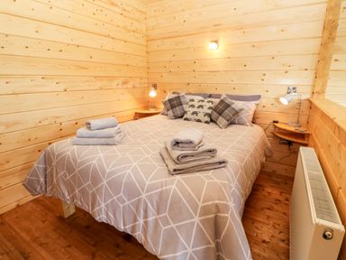 A bedroom with a double bed covered in a patterned duvet and pillows with towels on the bed and wooden walls at Badgers Sett in Winston near Staindrop