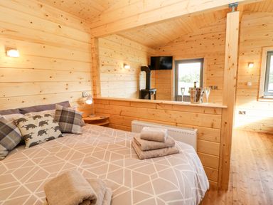 A bedroom with a bed towels and cushions next to a wood stove and a tv at Badgers Sett Winston near Staindrop