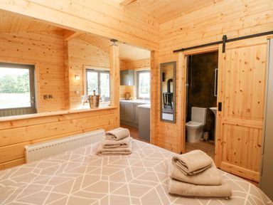 A bedroom with folded towels on the bed a door leading to a bathroom and a view of a kitchen at Badgers Sett in Winston near Staindrop