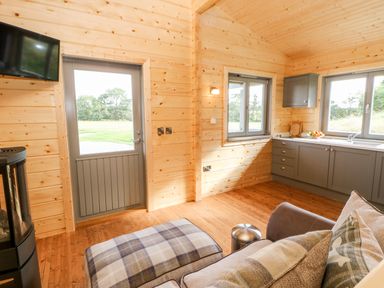 A small wooden living space with a sofa, ottoman, kitchen cabinets, windows, a door, and a wall-mounted TV at Badgers Sett in Winston near Staindrop