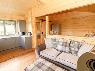 A living area with a sofa and cushions near a kitchen with cabinetry and appliances at Badgers Sett in Winston near Staindrop