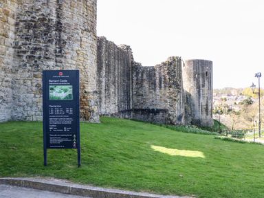 Stone walls of Barnard Castle with a sign showing information and green grass around the castle at Barnard Castle
