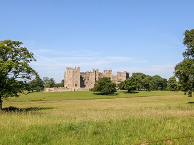 A stone castle surrounded by grass and trees under a blue sky at Badgers Sett in Winston near Staindrop