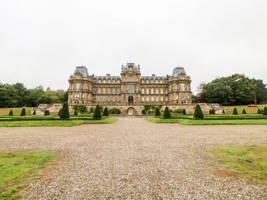 A large historic building with multiple windows and mansard roofs in front of a gravel pathway and landscaped garden with trimmed bushes