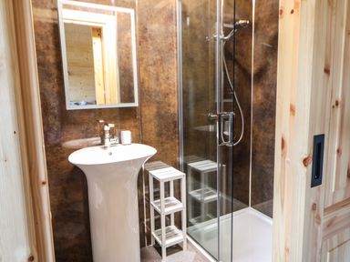 A bathroom with a pedestal sink mirror glass shower door and a small white shelving unit at Badgers Sett in Winston near Staindrop