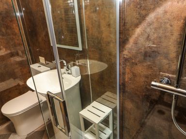 A bathroom with a toilet sink shower and a white stool behind glass at Badgers Sett in Winston near Staindrop