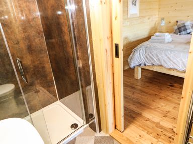 A shower with glass doors next to a wooden bedroom with a bed and folded towels at Badgers Sett in Winston near Staindrop