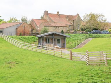 A small wooden cabin with a picnic table and fenced green grass area at Badgers Sett in Winston near Staindrop
