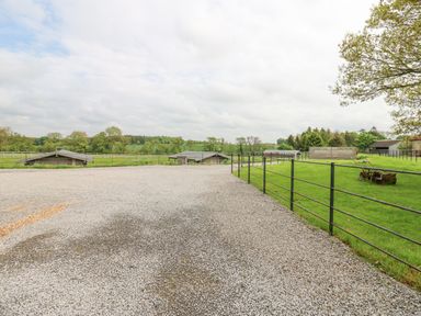 A gravel driveway with metal fences and grass fields with farm buildings in the background at Badgers Sett in Winston near Staindrop