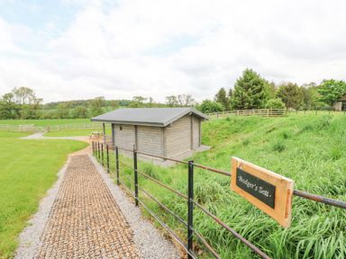 A pathway leading to a small wooden building with a fenced grassy area and a sign reading Badgers Sett Winston near Staindrop