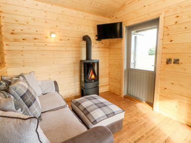 A wooden room with a door a wall-mounted TV a stove sofa and an ottoman with plaid cushions at Badgers Sett in Winston near Staindrop