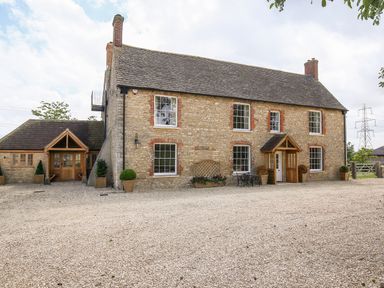A stone farmhouse with multiple windows and wooden doors with potted plants outside at Shifford Manor Farm in Shifford near Bampton Oxfordshire