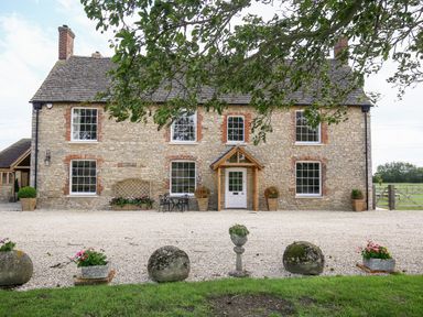 A stone house with a gravel driveway and flower pots at Shifford Manor Farm in Shifford near Bampton Oxfordshire