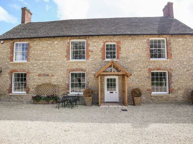 A stone house with six windows a white door with wooden porch and outdoor table and chairs at Shifford Manor Farm in Shifford near Bampton Oxfordshire