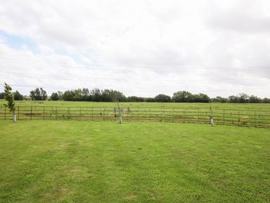 A green grassy field with a metal fence and small trees at Shifford Manor Farm in Shifford near Bampton Oxfordshire