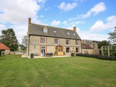 A stone house with windows chimneys and a patio with outdoor furniture surrounded by a lawn at Shifford Manor Farm Shifford near Bampton Oxfordshire