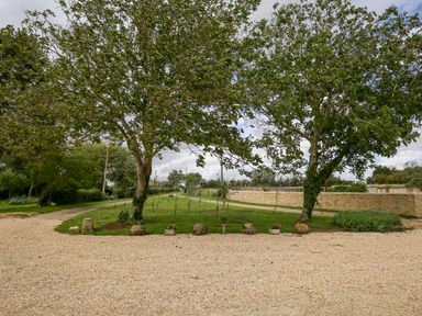 A gravel driveway with two trees and a lawn with stone decorations at Shifford Manor Farm in Shifford near Bampton Oxfordshire