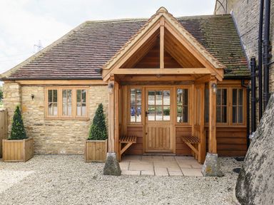 Exterior view of a stone building with a wooden porch and two planters with shrubs at Shifford Manor Farm in Shifford near Bampton Oxfordshire