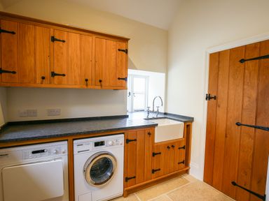 A laundry room with wooden cabinets washing machine dryer and a sink at Shifford Manor Farm in Shifford near Bampton Oxfordshire