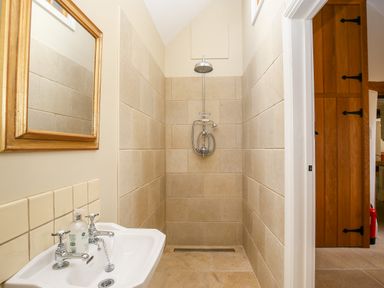 A shower area with tiled walls and showerhead next to a sink with taps and a mirror at Shifford Manor Farm in Shifford near Bampton Oxfordshire