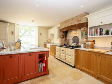 A kitchen with a large cream-colored stove under a brick arch and a red island with a knife block at Shifford Manor Farm Shifford near Bampton Oxfordshire