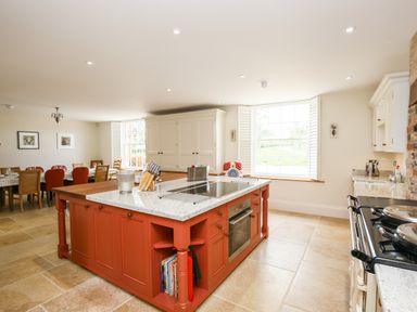 A kitchen with a red island counter and dining table with chairs at Shifford Manor Farm in Shifford near Bampton Oxfordshire