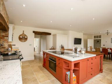 A kitchen with a large island with stovetop and oven a dining area with chairs and table in the background at Shifford Manor Farm in Shifford near Bampton Oxfordshire