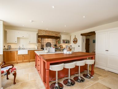 A kitchen with a large island and four white bar stools at Shifford Manor Farm in Shifford near Bampton Oxfordshire