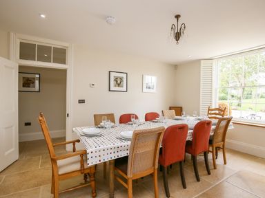 A dining room with a table set with plates and glasses surrounded by various chairs at Shifford Manor Farm in Shifford near Bampton Oxfordshire