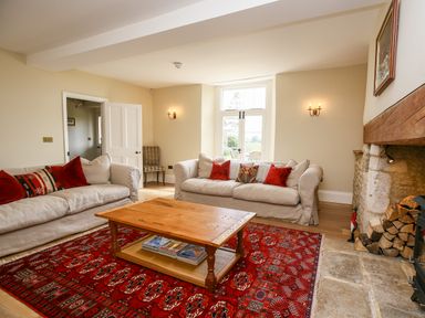 A living room with two sofas a wooden coffee table a fireplace and a red patterned rug at Shifford Manor Farm in Shifford near Bampton Oxfordshire