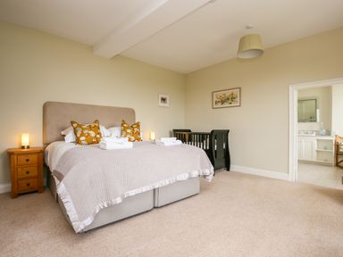 A bedroom with a double bed two bedside tables lamps a baby crib and an open door showing a bathroom at Shifford Manor Farm in Shifford near Bampton Oxfordshire