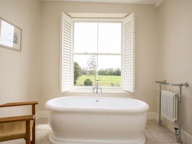 A bathroom with a freestanding bathtub in front of a window and a wooden chair at Shifford Manor Farm in Shifford near Bampton Oxfordshire