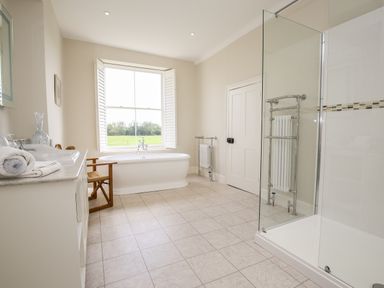 A bathroom with a freestanding bathtub near a window a glass shower enclosure a white vanity with folded towels and a wooden chair at Shifford Manor Farm Shifford near Bampton Oxfordshire