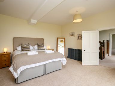 A bedroom with a double bed, bedside tables with lamps, a mirror, radiator, and an open door showing a staircase at Shifford Manor Farm in Shifford near Bampton Oxfordshire