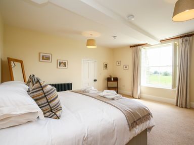 A bedroom with a bed pillows wall mirror small wooden shelf and a large window at Shifford Manor Farm Shifford near Bampton Oxfordshire