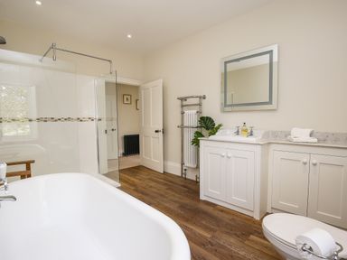A bathroom with a bathtub a shower a sink with a mirror and cabinets a toilet and wooden flooring at Shifford Manor Farm in Shifford near Bampton Oxfordshire