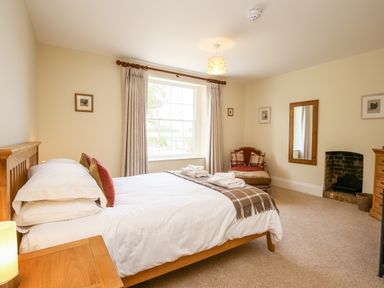 A bedroom with a double bed wooden furniture a window with curtains an armchair and a fireplace at Shifford Manor Farm Shifford near Bampton Oxfordshire
