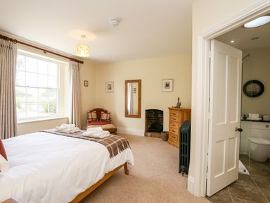 A bedroom with a bed next to a window a chair a wooden dresser a small fireplace and an open door leading to a bathroom at Shifford Manor Farm in Shifford near Bampton Oxfordshire