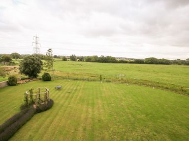 A large open grassy field with a circular wooden plant support and a table with chairs at Shifford Manor Farm in Shifford near Bampton Oxfordshire