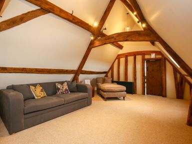 An attic room with exposed wooden beams a gray sofa with colorful cushions and a patterned lounge chair at Shifford Manor Farm Shifford near Bampton Oxfordshire