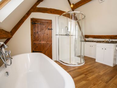 A bathroom with a white bathtub a glass shower enclosure a wooden door and white cabinets at Shifford Manor Farm in Shifford near Bampton Oxfordshire