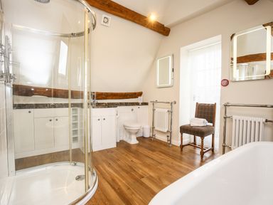 A bathroom with a corner shower, toilet, chair with towels, two illuminated mirrors, and wooden floor at Shifford Manor Farm in Shifford near Bampton Oxfordshire