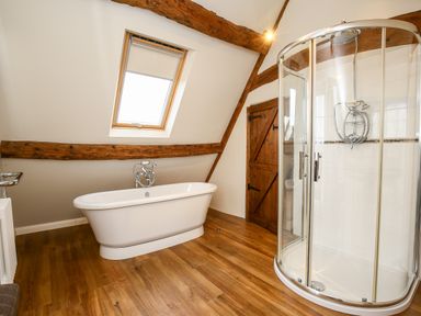 A bathroom with a freestanding bathtub, a glass-enclosed shower, a wooden door, a skylight window, and exposed wooden beams at Shifford Manor Farm in Shifford near Bampton Oxfordshire