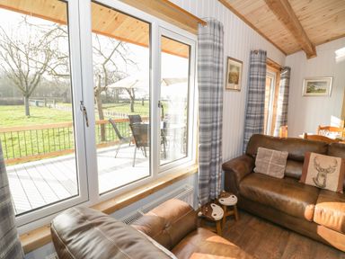 A living room with brown leather sofas cushions small stools dining table and large windows with a view of a garden at Top Style Orchard in Hallow