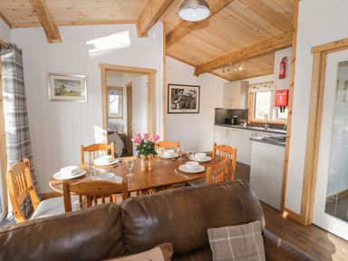 A dining area with a wooden table set with dishes and glasses next to a kitchen with white cabinets and a brown leather sofa at Top Style Orchard in Hallow